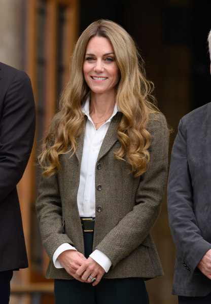 Kate Middleton appears at an event with long honeyblonde hair. She wears a white shirt and jacket.